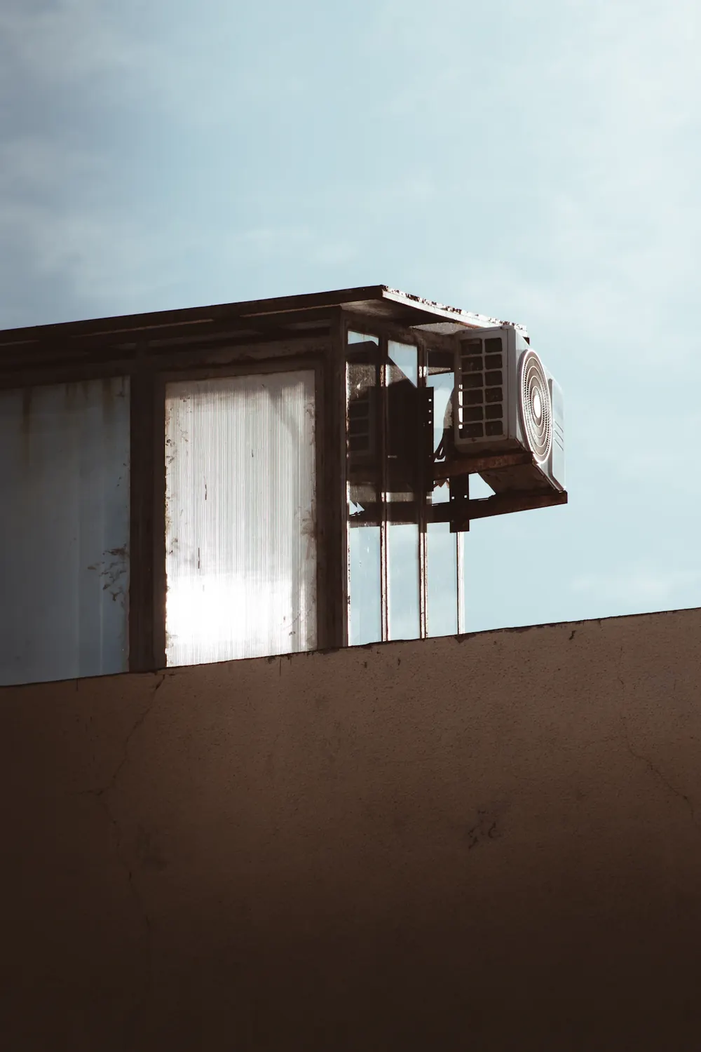 A wall air-conditioning unit on a sun-bleached parapet against a pale sky