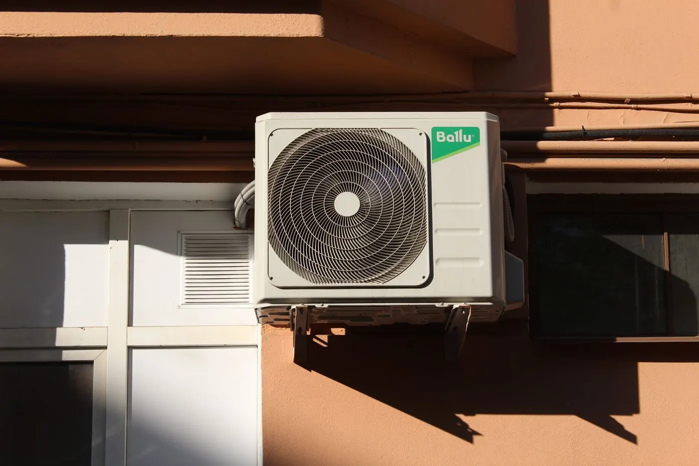 A wall-mounted condensing unit on a sunlit apartment wall