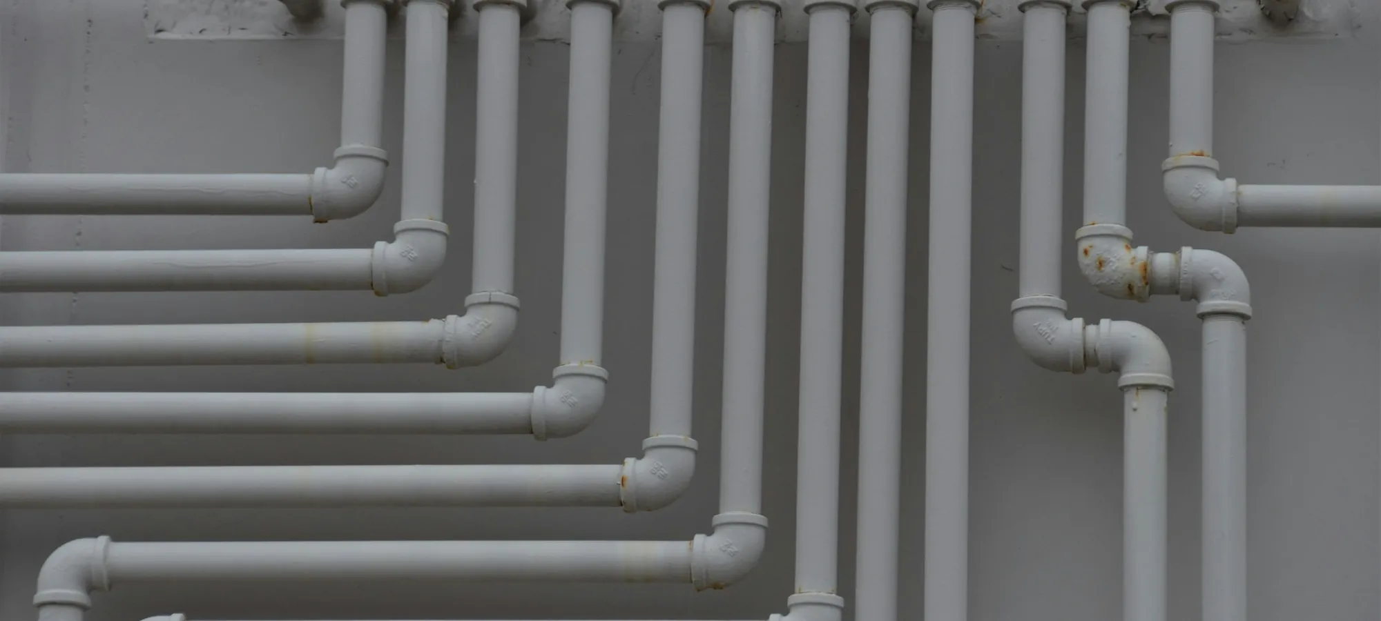 A wall of white-painted pipe risers turning in ranks across a mechanical room.