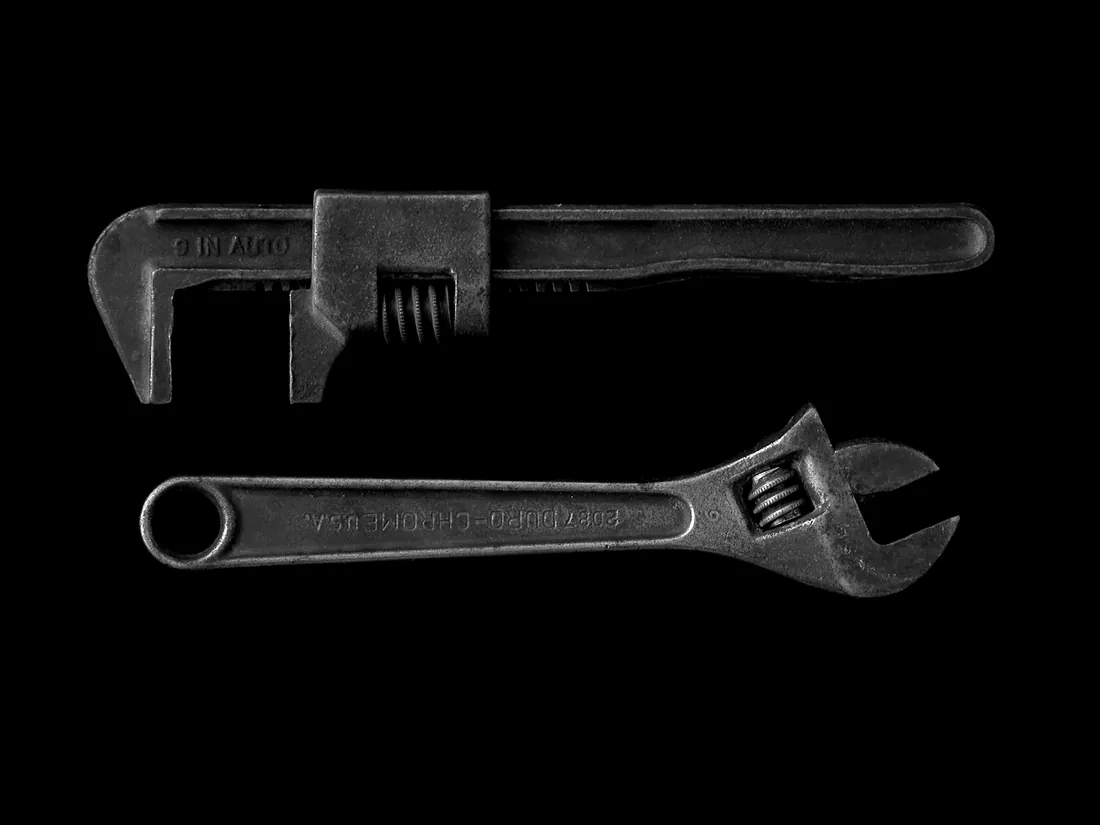 Two worn adjustable wrenches laid on a black surface.